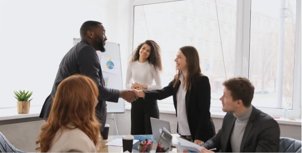 Business meeting with two people sitting down looking at people standing up shaking hands