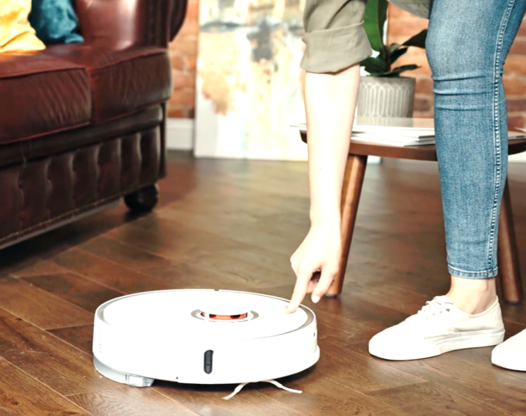 Woman leaning down to turn on a robot vacuum cleaner on a wooden floor